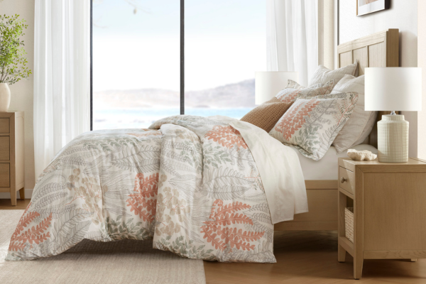 California coastal winter bedroom styled with botanical bedding in warm neutral tones, layered textures, and natural wood accents overlooking a serene ocean view.