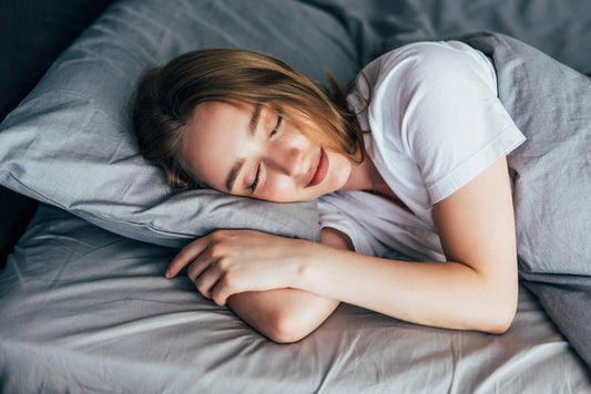 A woman sleeping comfortably on the bed with gray-colored beddings.