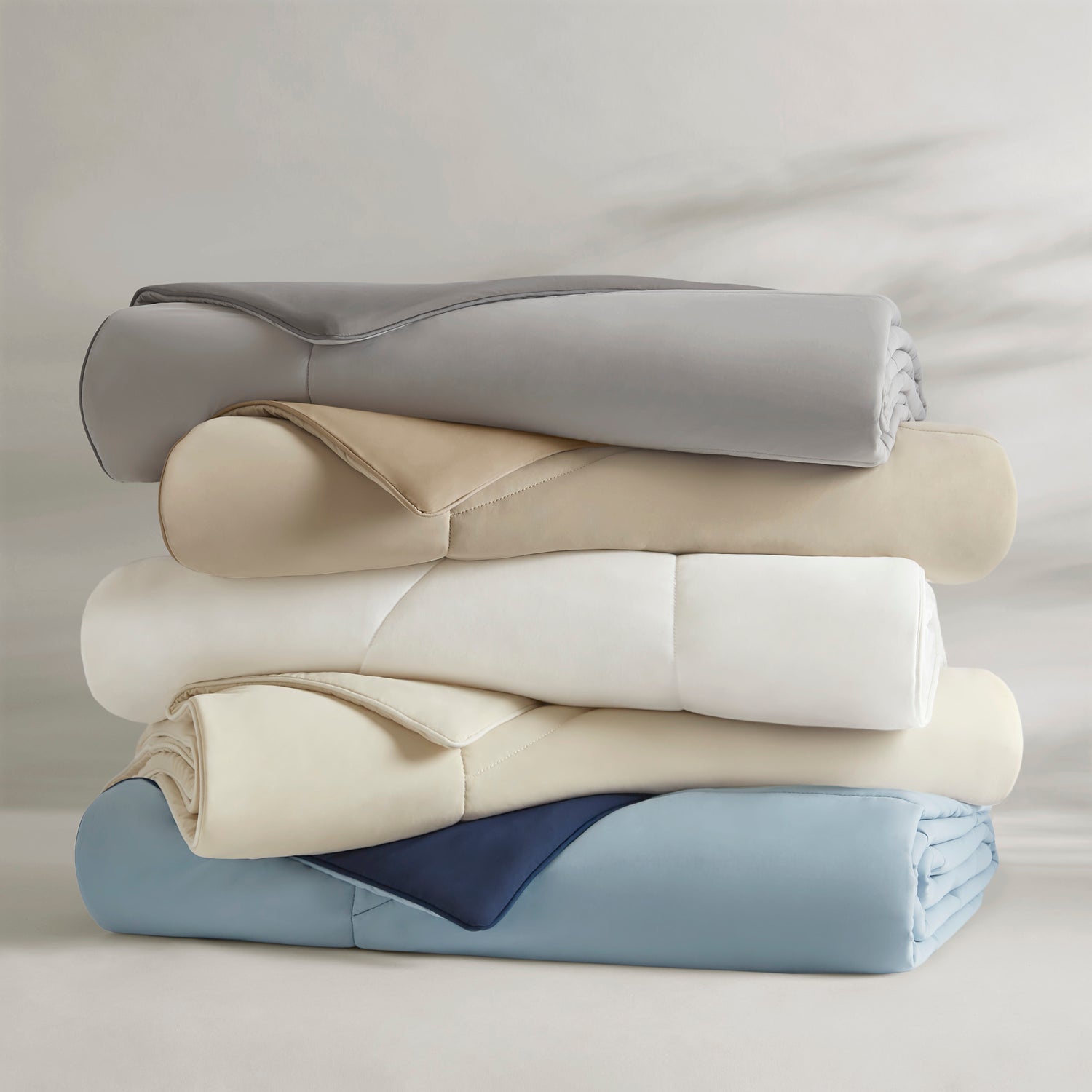 Stack of folded premium bedding in gray, beige, white, cream, and blue.