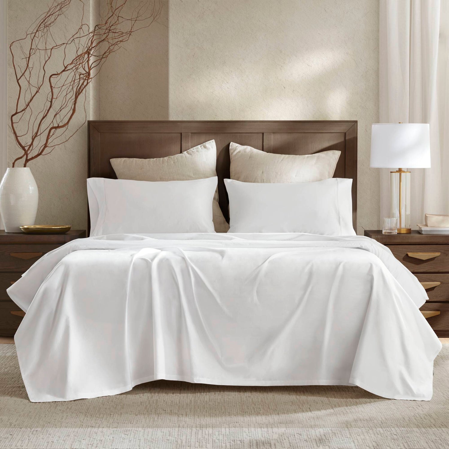 Luxurious white bedding set on a wooden bed, featuring smooth, sustainable fabric, two large pillows, and a neatly draped comforter.