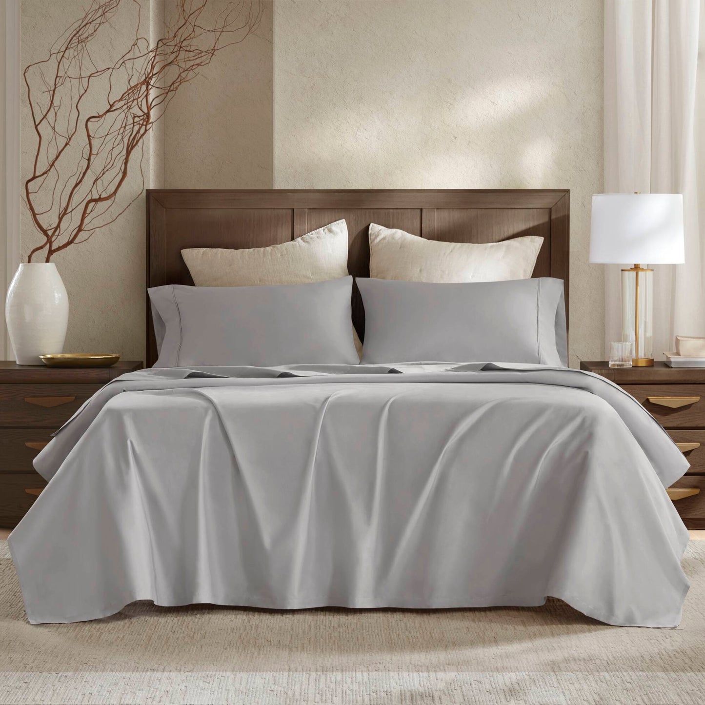 High-end gray bedding set on a wooden bed, featuring smooth, sustainable fabric, with matching pillows and a coastal-inspired design.