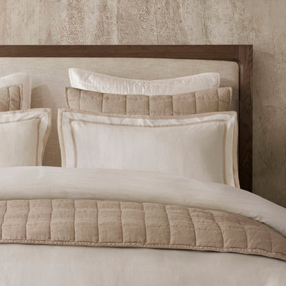 Luxury bedding with beige and white tones, featuring soft, quilted textures and layered pillows, inspired by the California coastline.