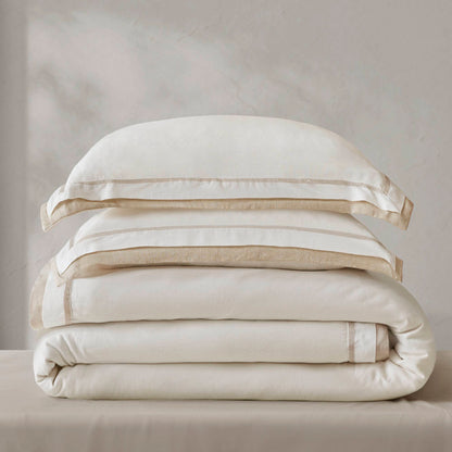 Cream-colored designer bedding set with subtle beige trim, neatly folded, showcasing soft, sustainable materials.